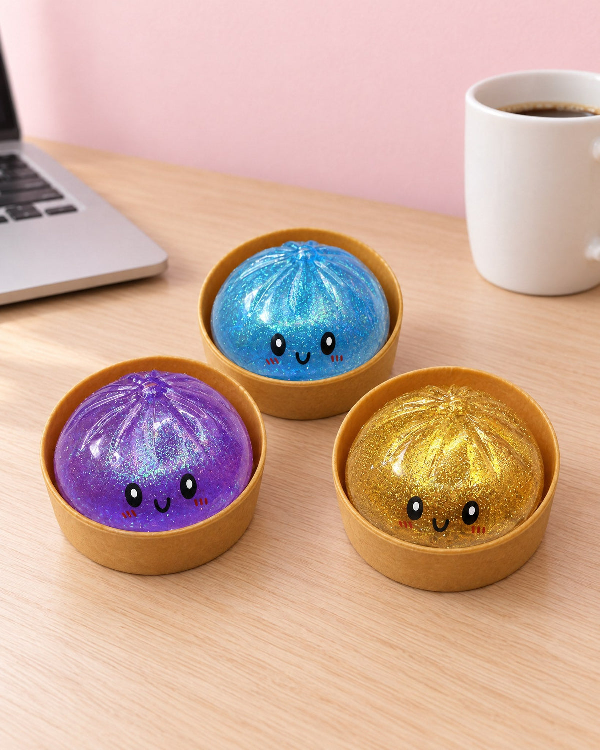 Three Sparkle Bao glitter buns in their steamer cups on a desk, next to a laptop