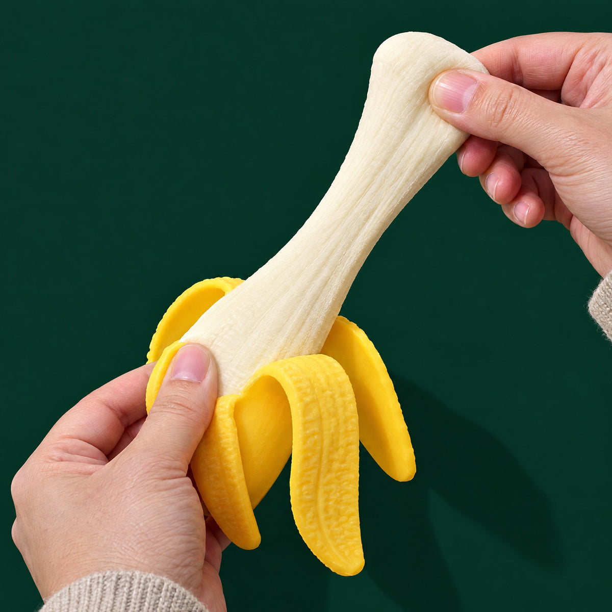 Two adult hands stretching the pale banana of the squishy toy while its yellow peel hangs down
