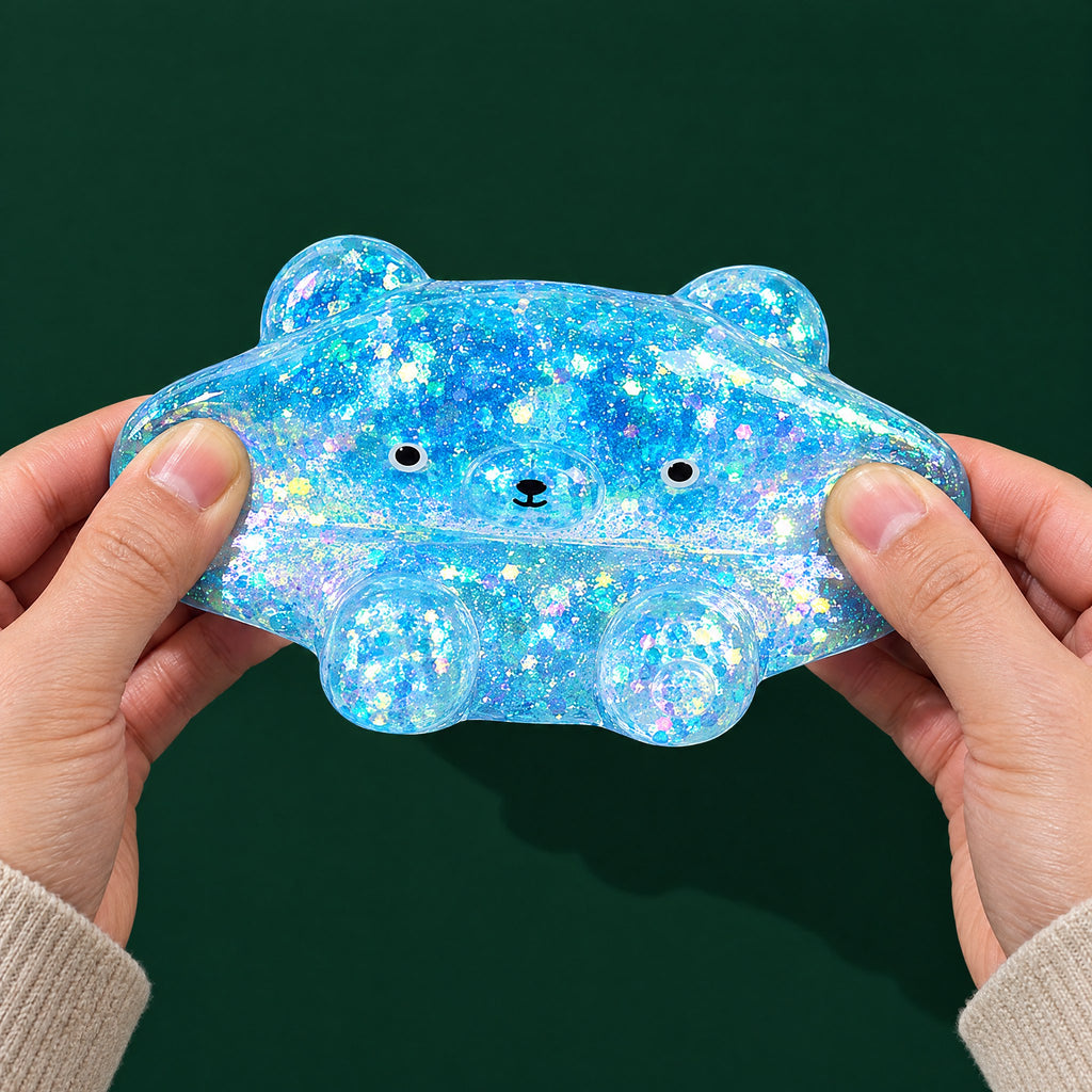 Two adult hands gently stretching the blue glitter-gel bear squishy sideways on a dark green background