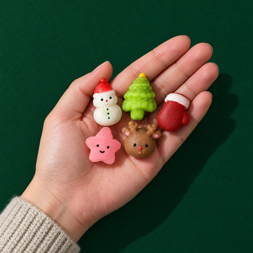 Open adult hand holding five tiny Christmas squishies: snowman, tree, mitten, pink star and reindeer