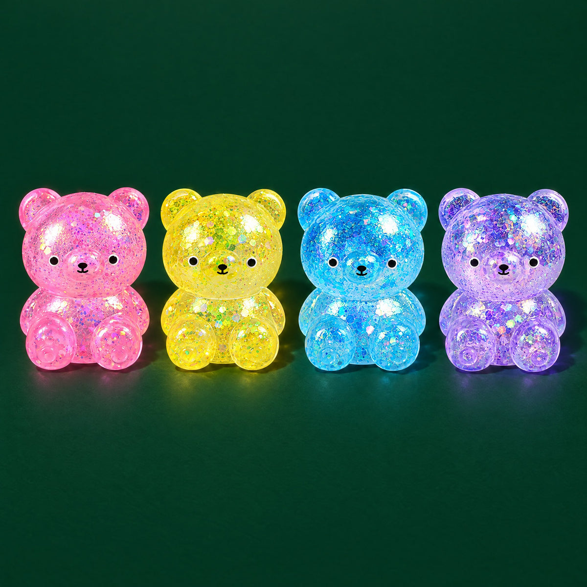 Pink, yellow, blue and purple glitter-gel bear squishies sitting in a row on a dark green stage
