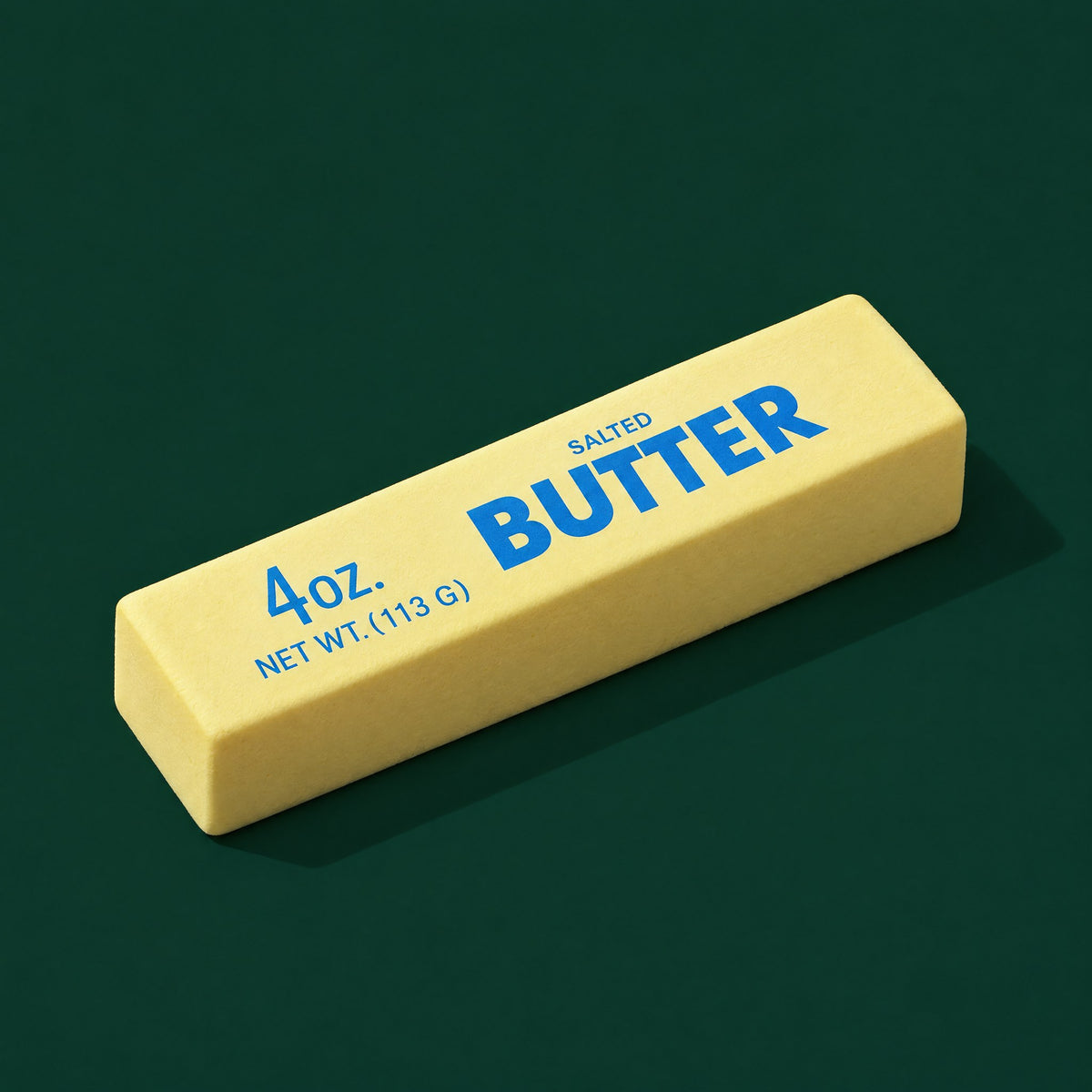 The Butter Stick: pale yellow foam squishy printed 4oz. Salted Butter, lying at an angle on dark green