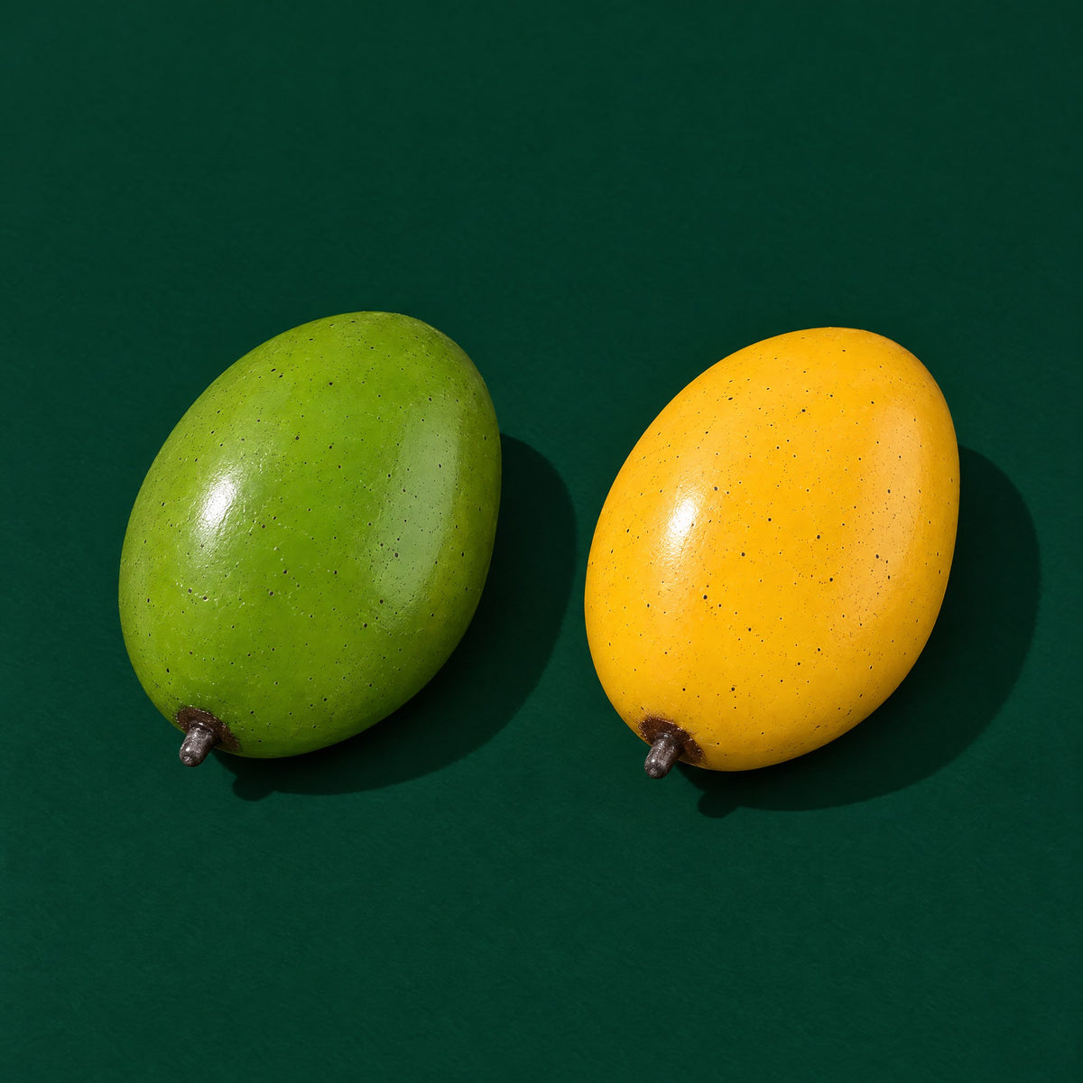 Two Mood Mango squishies on a dark green stage: one leaf green (cool), one golden yellow (warmed)