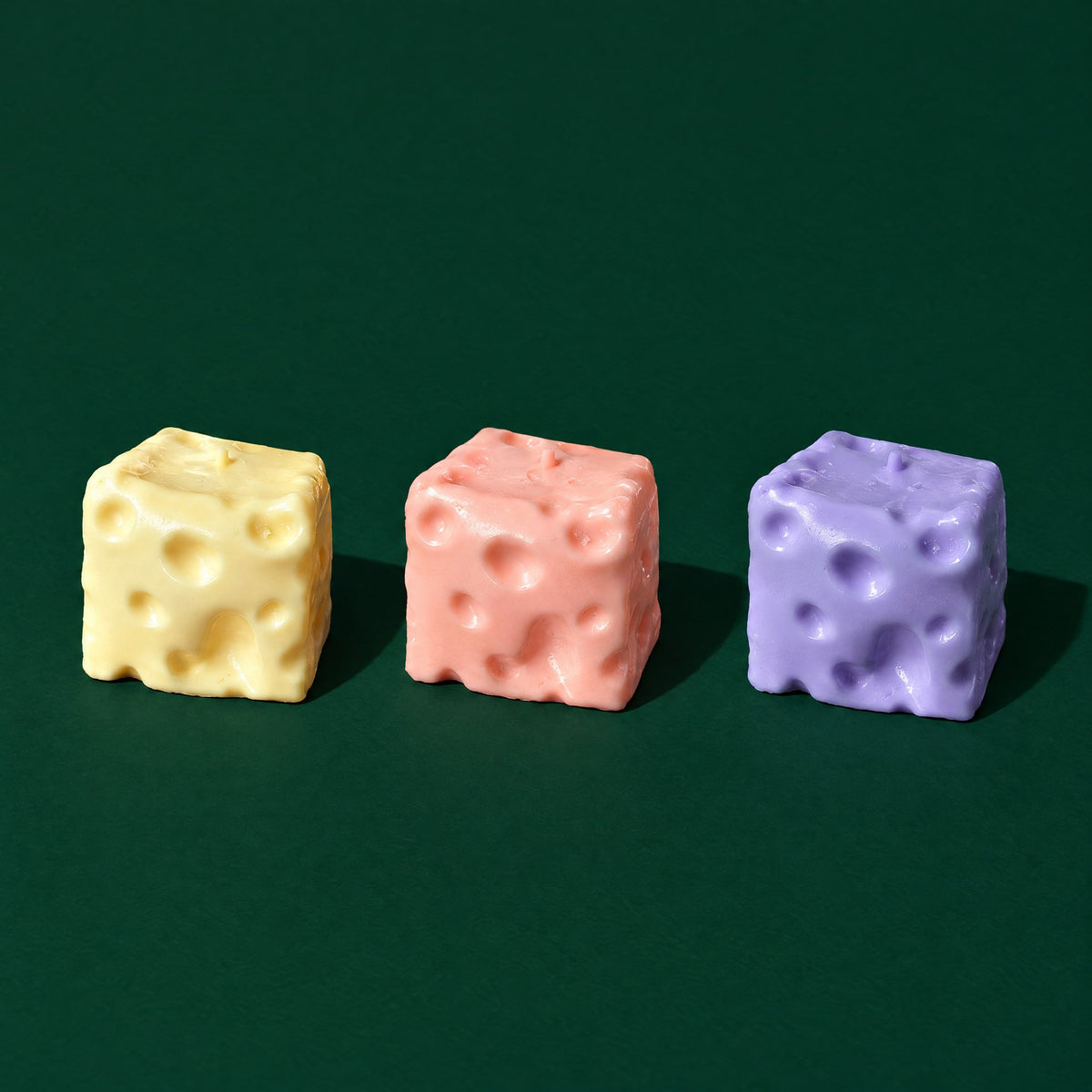 Yellow, pink and blueberry purple Dent Cheese squishy cubes with Swiss-cheese holes on a dark green stage