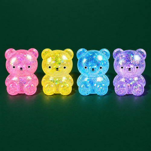 Pink, yellow, blue and purple glitter-gel bear squishies sitting in a row on a dark green stage