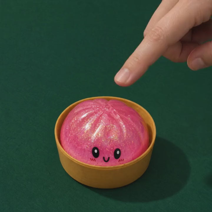 A finger presses the pink Sparkle Bao squishy in its cup and the glitter swirls