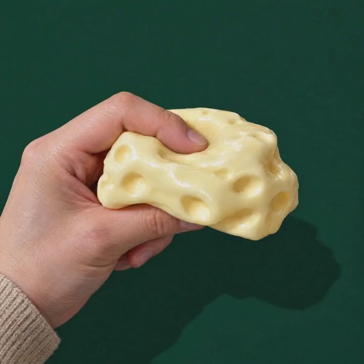 A thumb presses into the moldable Dent Cheese squishy and the thumbprint stays