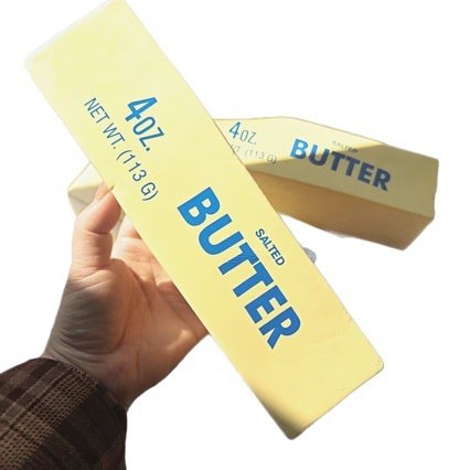 Real photo: a hand holding up the foam butter-stick squishy, with a second stick behind it