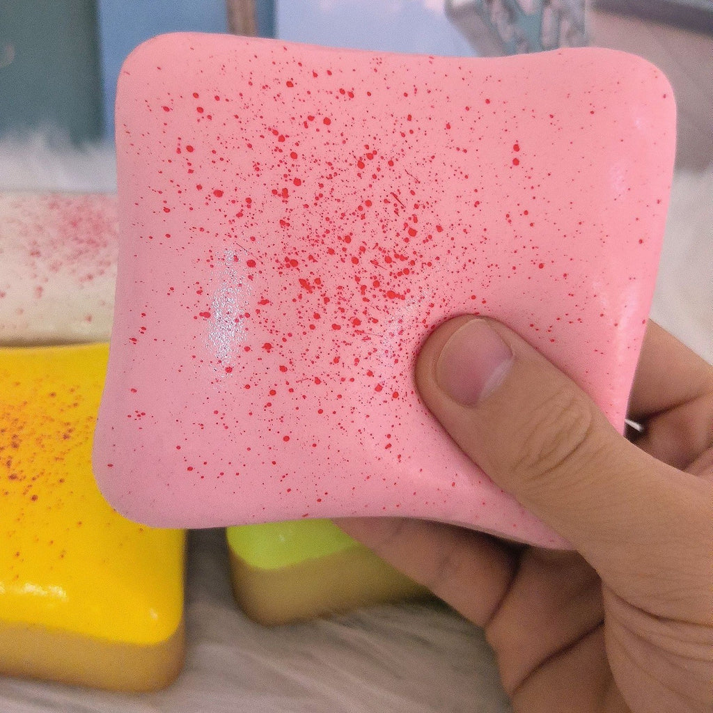 Real photo: a thumb presses into the pink speckled strawberry toast squishy, showing its hand size