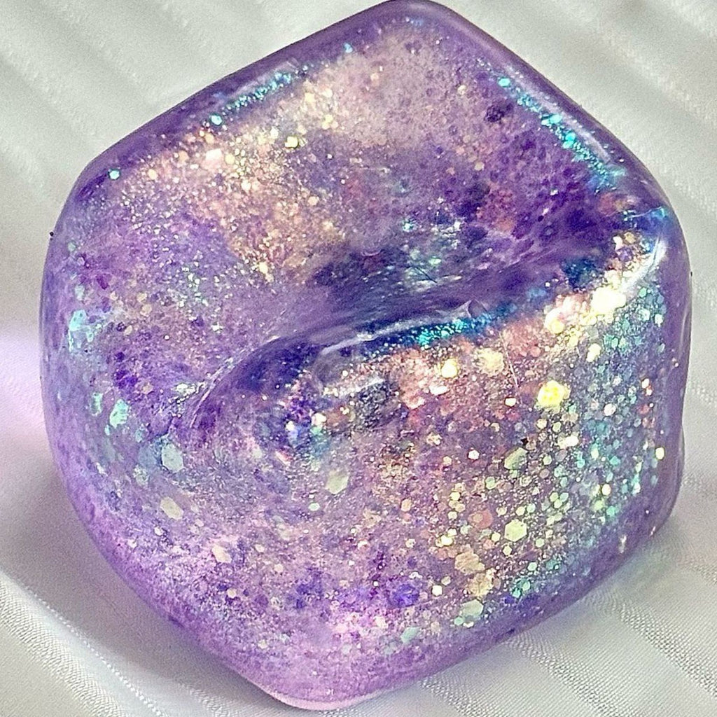 Real photo: glitter purple Crystal Ice cube with a pressed dent in its top, on white fabric