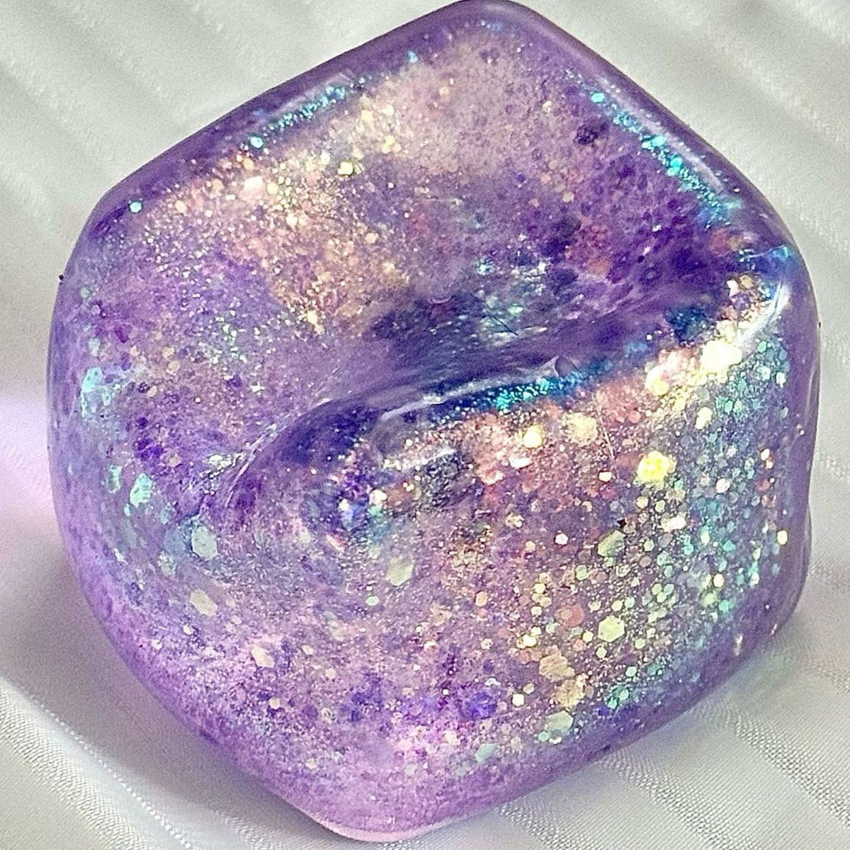 Real photo: glitter purple Crystal Ice cube with a pressed dent in its top, on white fabric