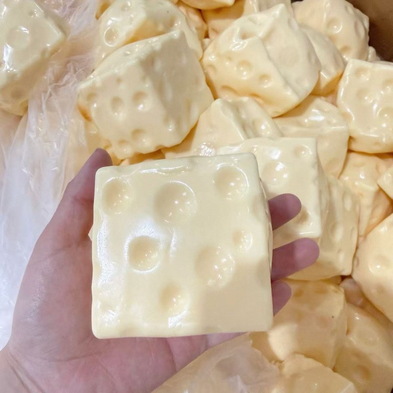 Real photo: yellow Dent Cheese cube with Swiss-cheese holes on an open adult hand
