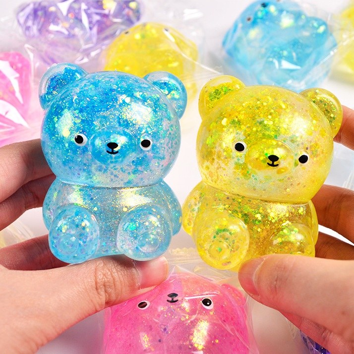 Real photo: blue and yellow glitter-gel bear squishies held up between adult fingers