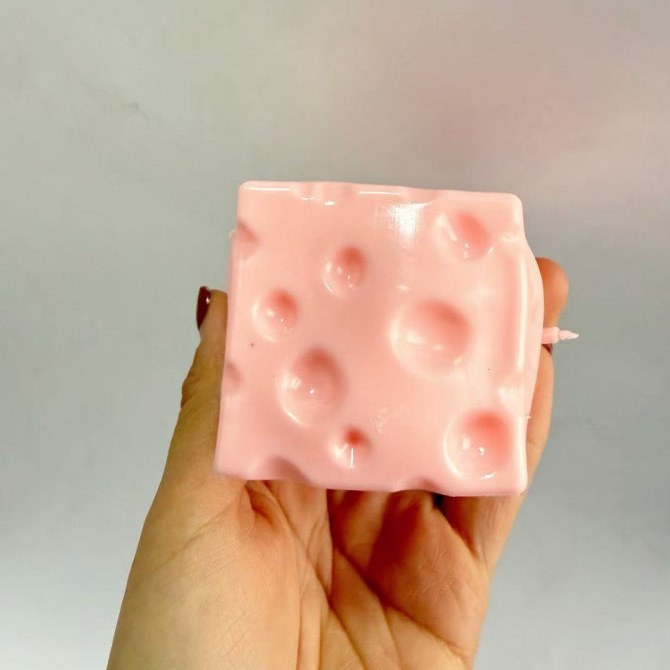 Real photo: pink Dent Cheese cube with Swiss-cheese holes held in a hand