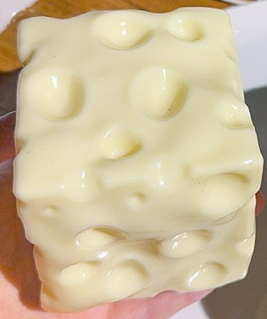 Real supplier photo: close-up of the pale yellow Swiss-cheese squishy cube held in a hand
