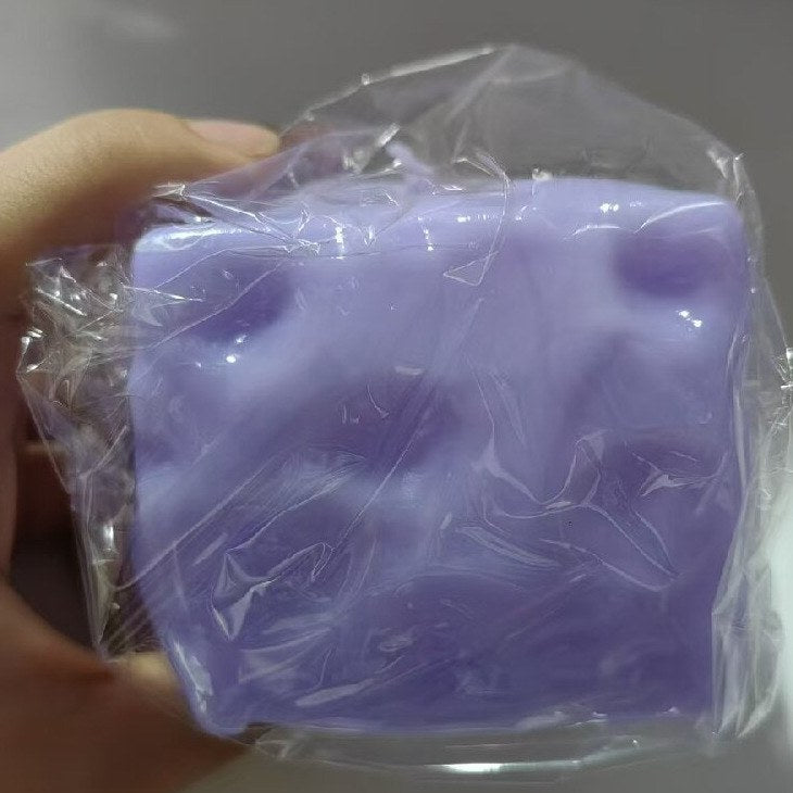 Real photo: blueberry purple Dent Cheese cube in a clear plastic wrap, held in a hand